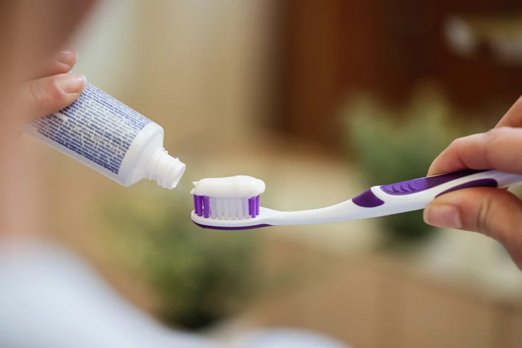 Close-up of a person applying toothpaste to a toothbrush, emphasizing proper dental care routines for protecting tooth enamel, as recommended by Rim Point Dental.